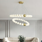 Above a cream boucle sofa and a potted plant, this Clérachic chandelier has two offset rings of lit white globes on brass fittings.