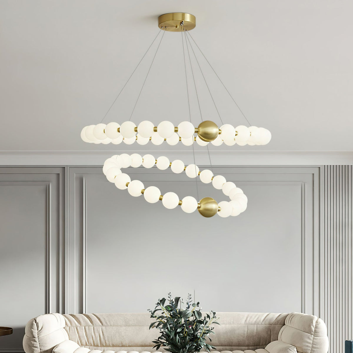 Above a cream boucle sofa and a potted plant, this Clérachic chandelier has two offset rings of lit white globes on brass fittings.
