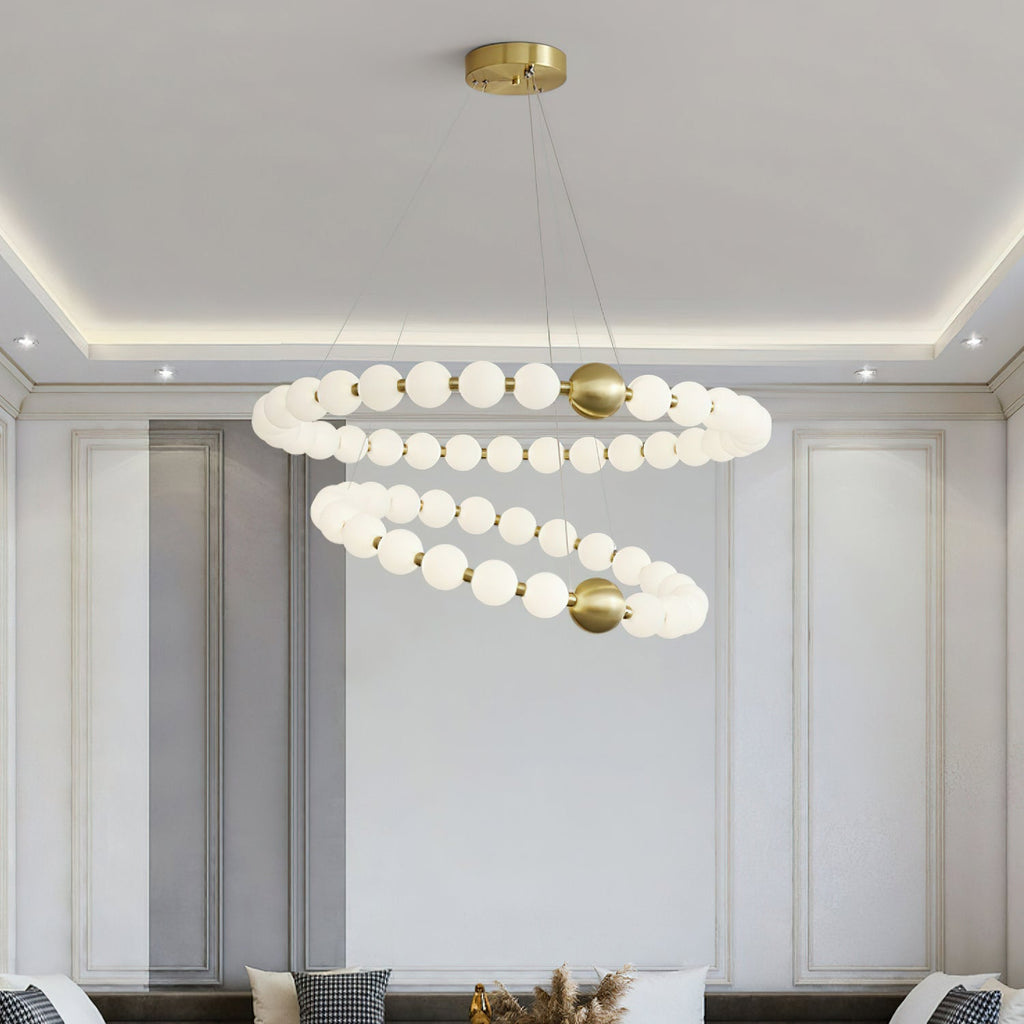 Close under a cove-lit ceiling, this Clérachic chandelier shows both globe rings with brass spheres between the beads.