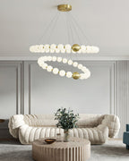 A two-ring Clérachic chandelier hangs above a low round wooden coffee table and a cream sofa with a green plant.