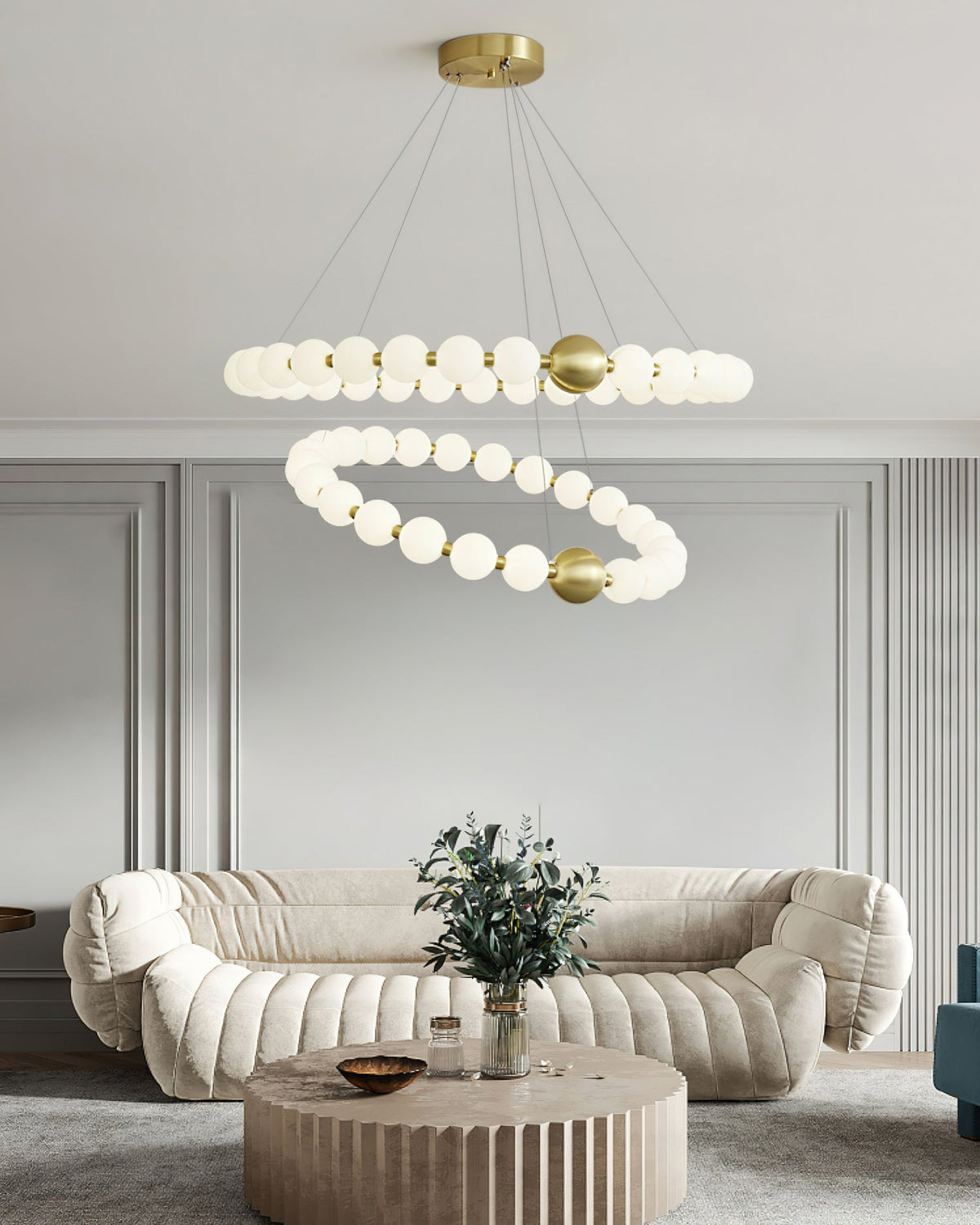 A two-ring Clérachic chandelier hangs above a low round wooden coffee table and a cream sofa with a green plant.