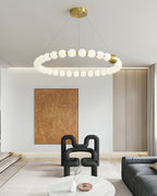 A single-ring Clérachic chandelier of white globes hangs in a bright room with a sculptural black chair and a marble table.