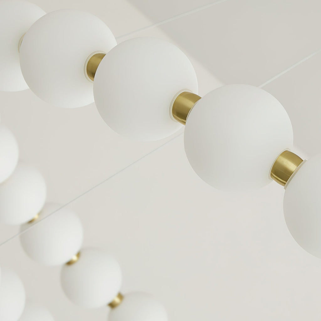 Close view of frosted white globes strung between small brass collars on this Clérachic chandelier.