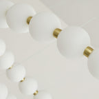 Close view of frosted white globes strung between small brass collars on this Clérachic chandelier.