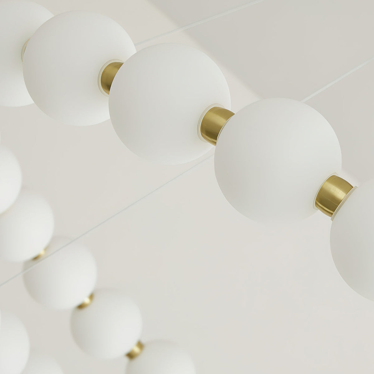 Close view of frosted white globes strung between small brass collars on this Clérachic chandelier.