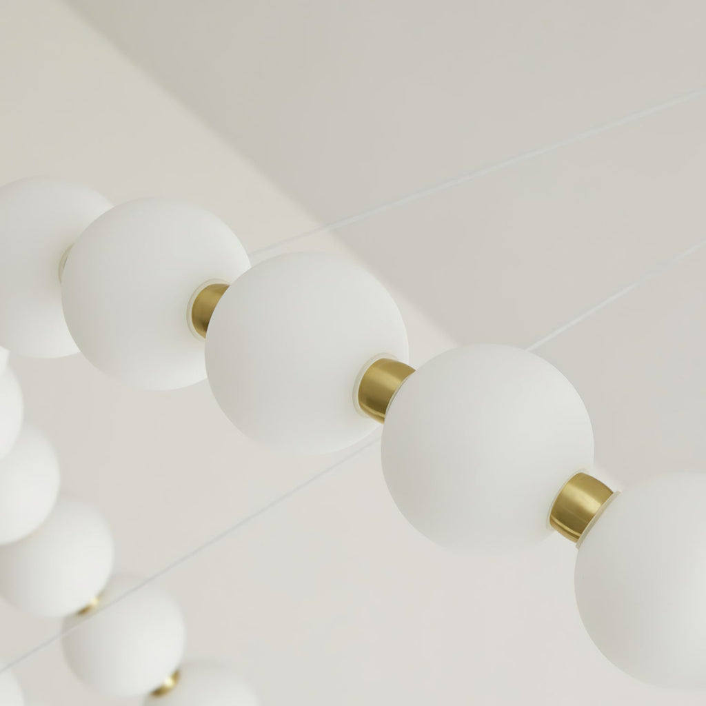 Looking up along a strand of frosted white globes and brass collars on this Clérachic chandelier.