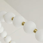 Looking up along a strand of frosted white globes and brass collars on this Clérachic chandelier.