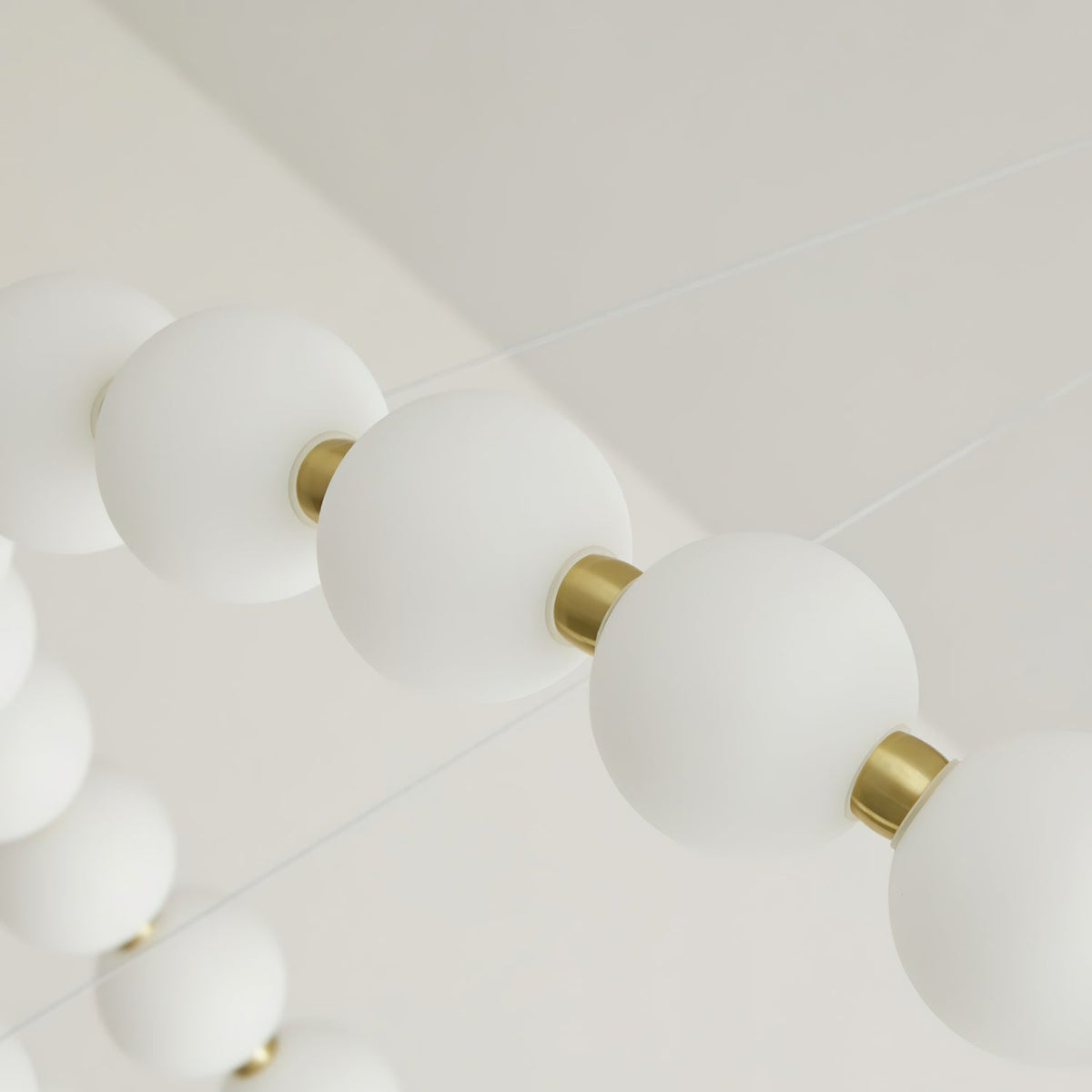 Looking up along a strand of frosted white globes and brass collars on this Clérachic chandelier.