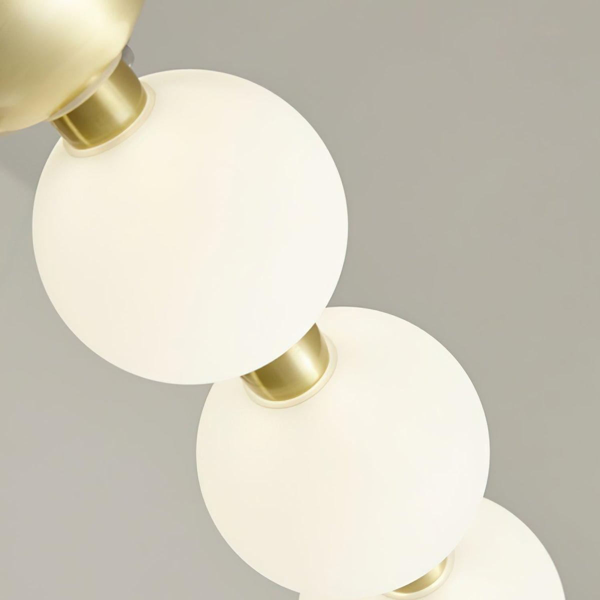 Close view of two lit globes glowing warm white on a brass collar, from this Clérachic chandelier.