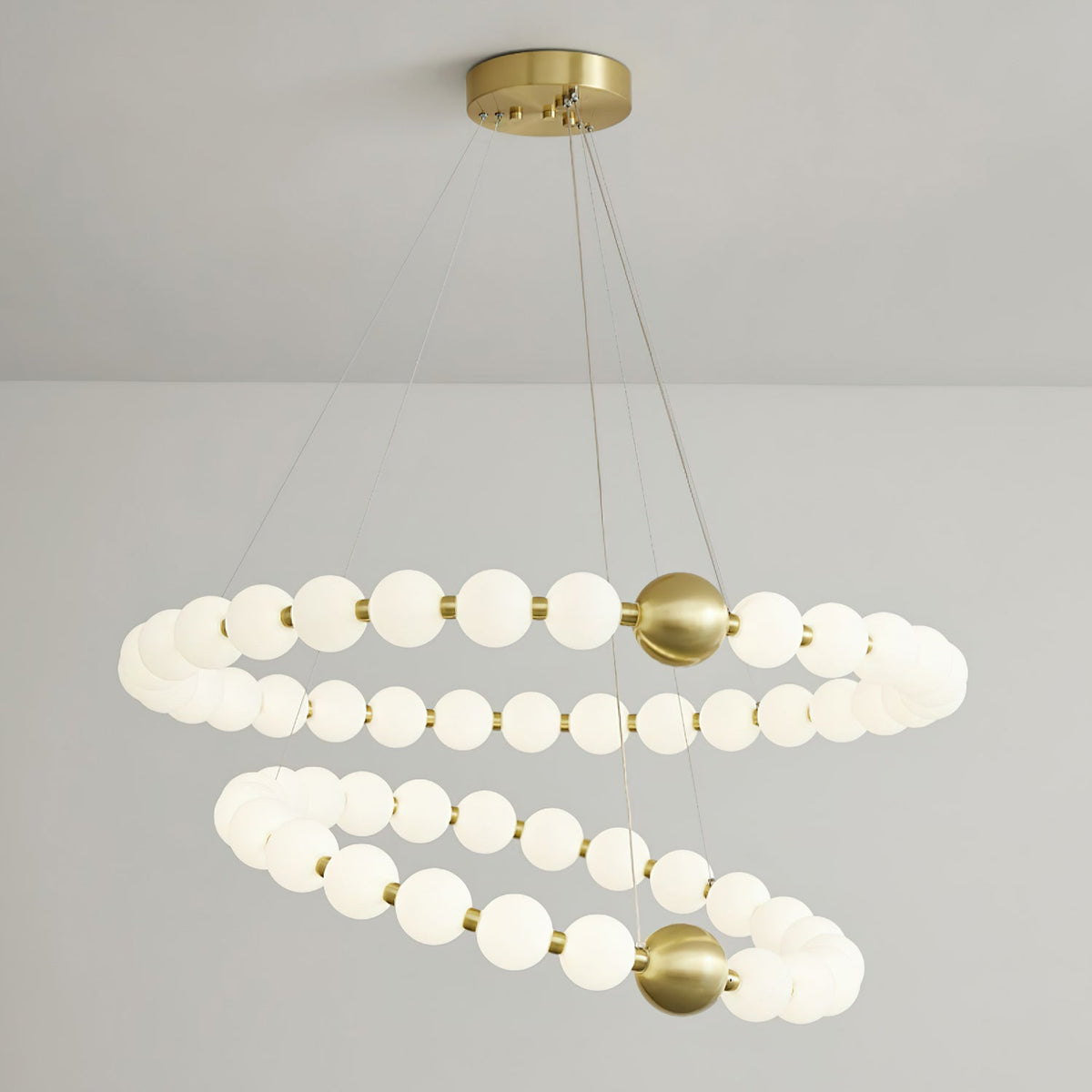 A two-ring Clérachic chandelier lit against a grey wall, with a round brass ceiling plate and fine suspension cables.