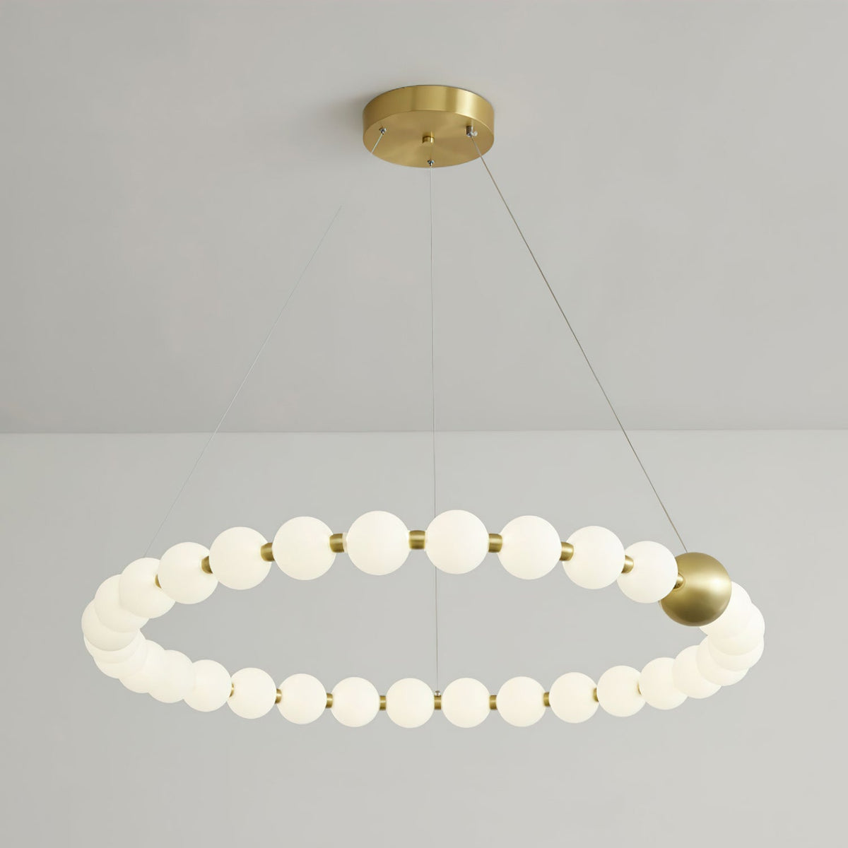 A single large ring of lit white globes with one brass sphere, on a Clérachic chandelier hung from three fine cables.