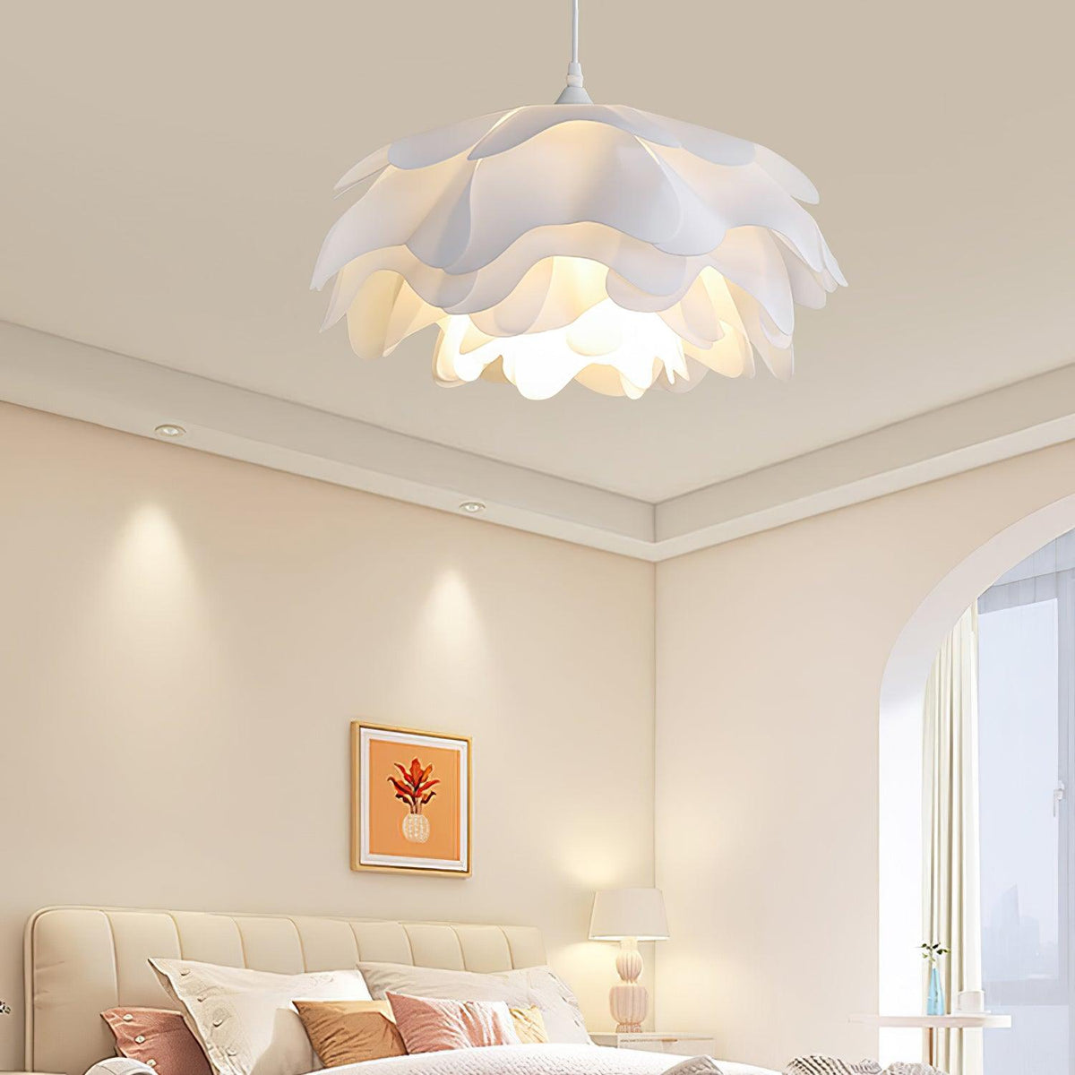 A Clérachic layered-petal pendant lit above a cream bedroom with a tufted headboard, a framed print and a bedside lamp.