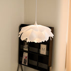 Another angle of a Clérachic petal pendant in a corner, its curved white layers casting a warm glow beside a dark display shelf.