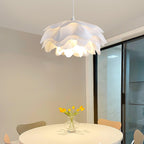 Warm light from a Clérachic pendant with white petals, hung above a round table with yellow tulips beside a sliding glass door.