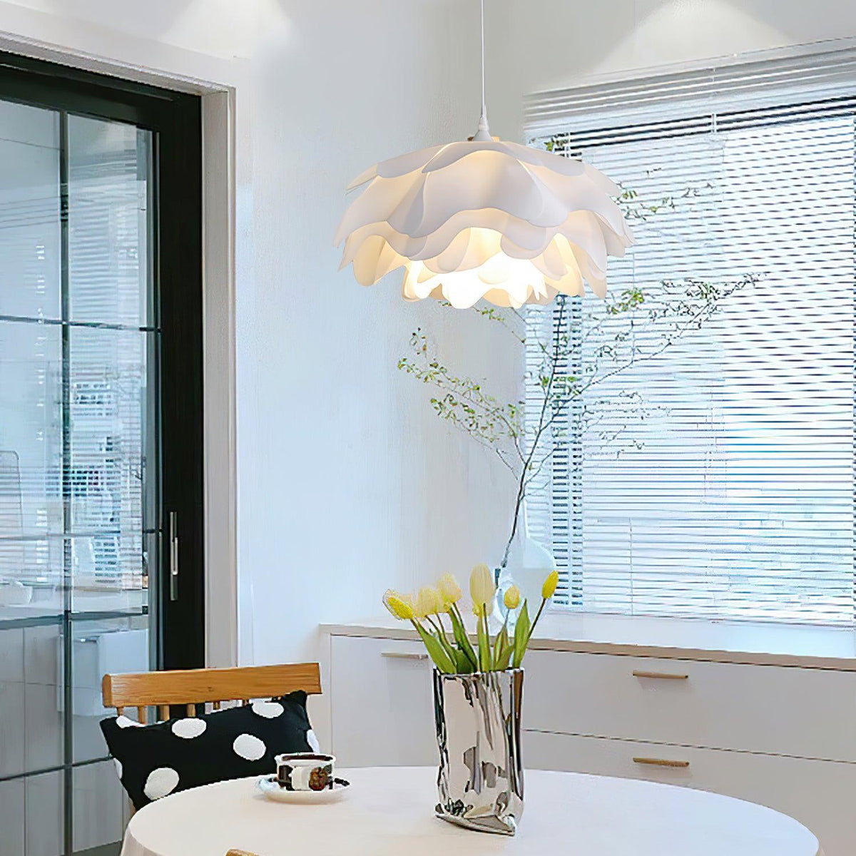A Clérachic pendant with ruffled white petals in a bright room with louvred blinds and tulips in a silver vase.