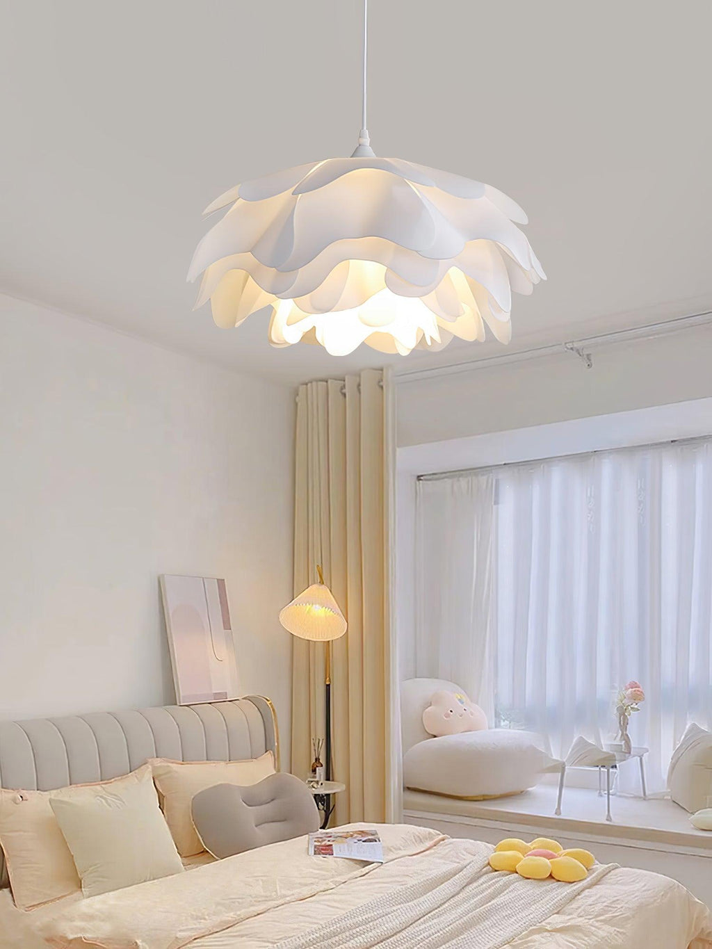 Clérachic petal pendant lit above a bedroom with a grey headboard, a floor lamp and sheer curtains over a window seat.