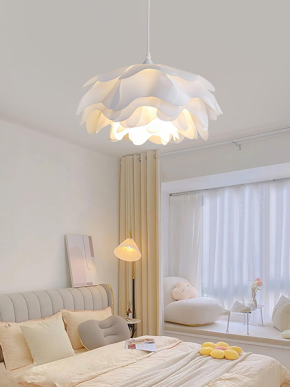 Clérachic petal pendant lit above a bedroom with a grey headboard, a floor lamp and sheer curtains over a window seat.