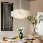 This Clérachic pendant's ruffled lower petals shown above a dining table, with louvred shutters and a vase of white flowers.