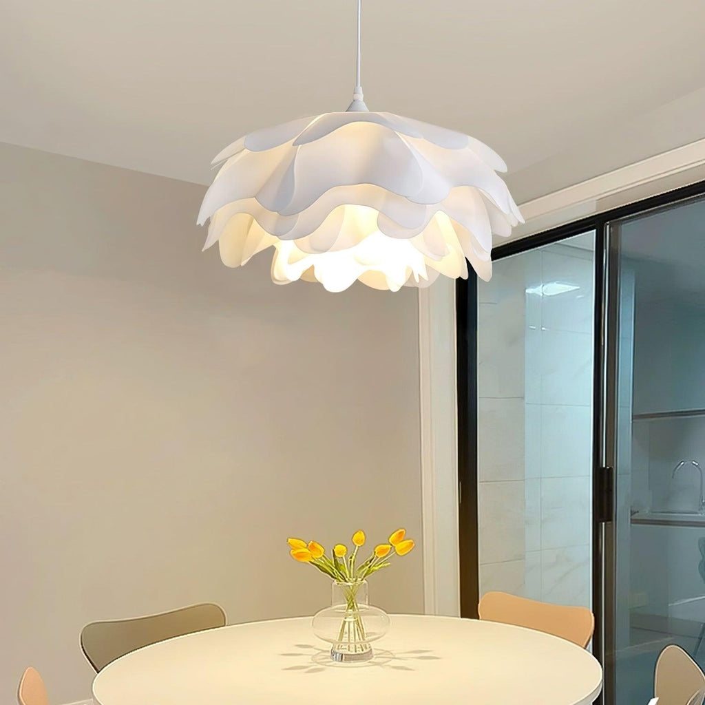 Lit Clérachic pendant with tiered petals above a round table with yellow tulips, near a dark-framed glass door.