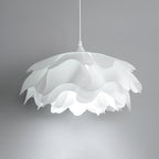 Underside view of this Clérachic pendant against a grey wall, showing the overlapping white petals and the bulb glowing within.