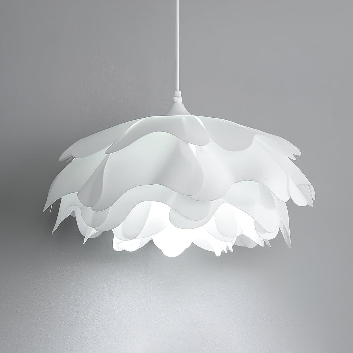 Underside view of this Clérachic pendant against a grey wall, showing the overlapping white petals and the bulb glowing within.