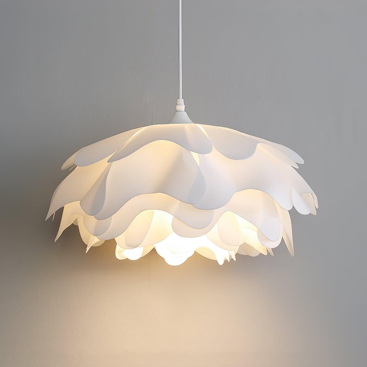 Close view of a lit Clérachic pendant with broad scalloped petals, glowing warmly against a grey wall.