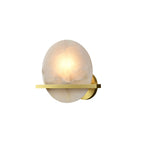 Clérachic White Alabaster Wall Sconce lit on a plain white studio background, its brass bar crossing the glowing stone disc.