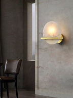 The Clérachic White Alabaster Wall Sconce lit on a stone-clad dining wall, casting a soft halo beside a dark leather chair.