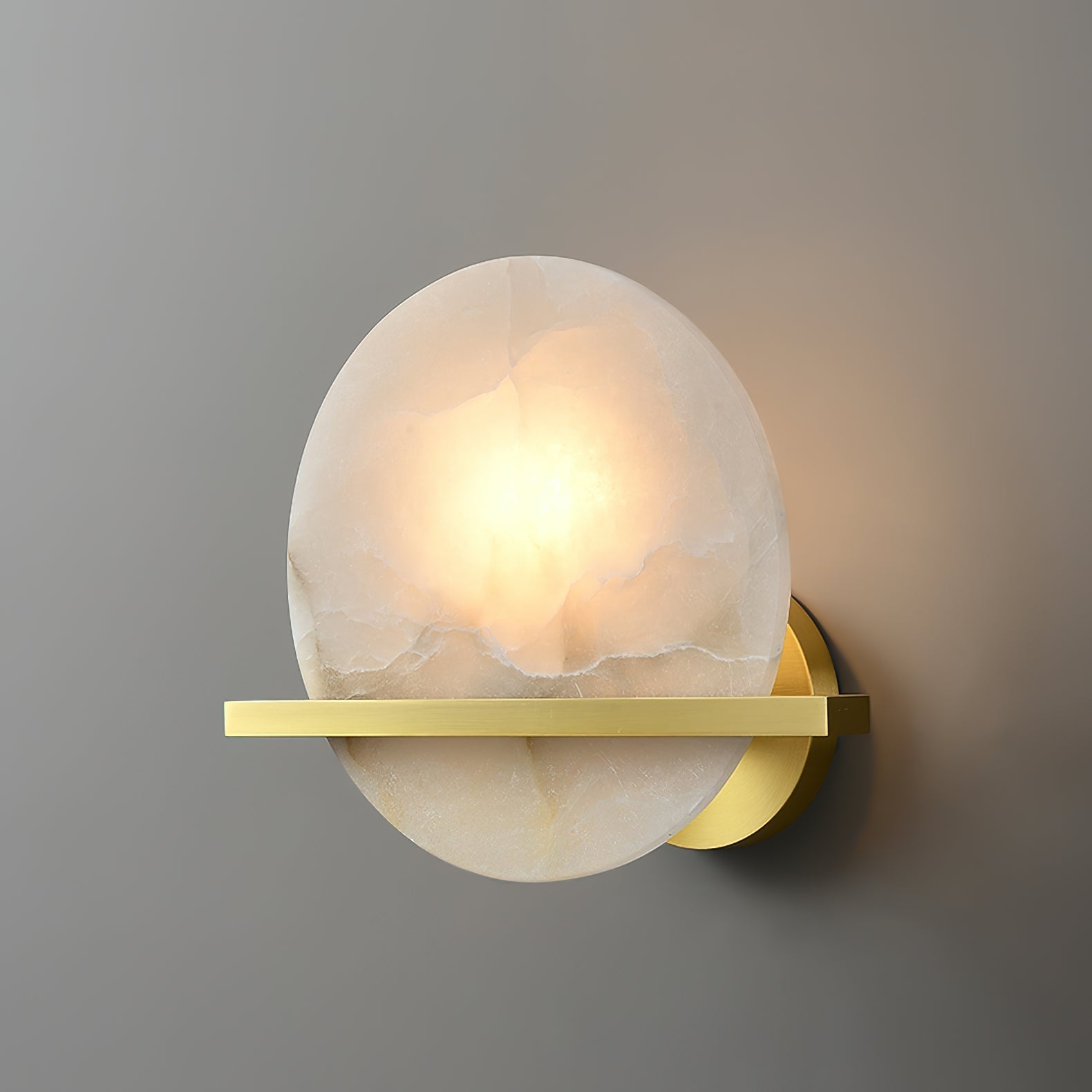 Clérachic White Alabaster Wall Sconce lit head-on against a grey wall, the bulb glowing through the stone with no visible glare.
