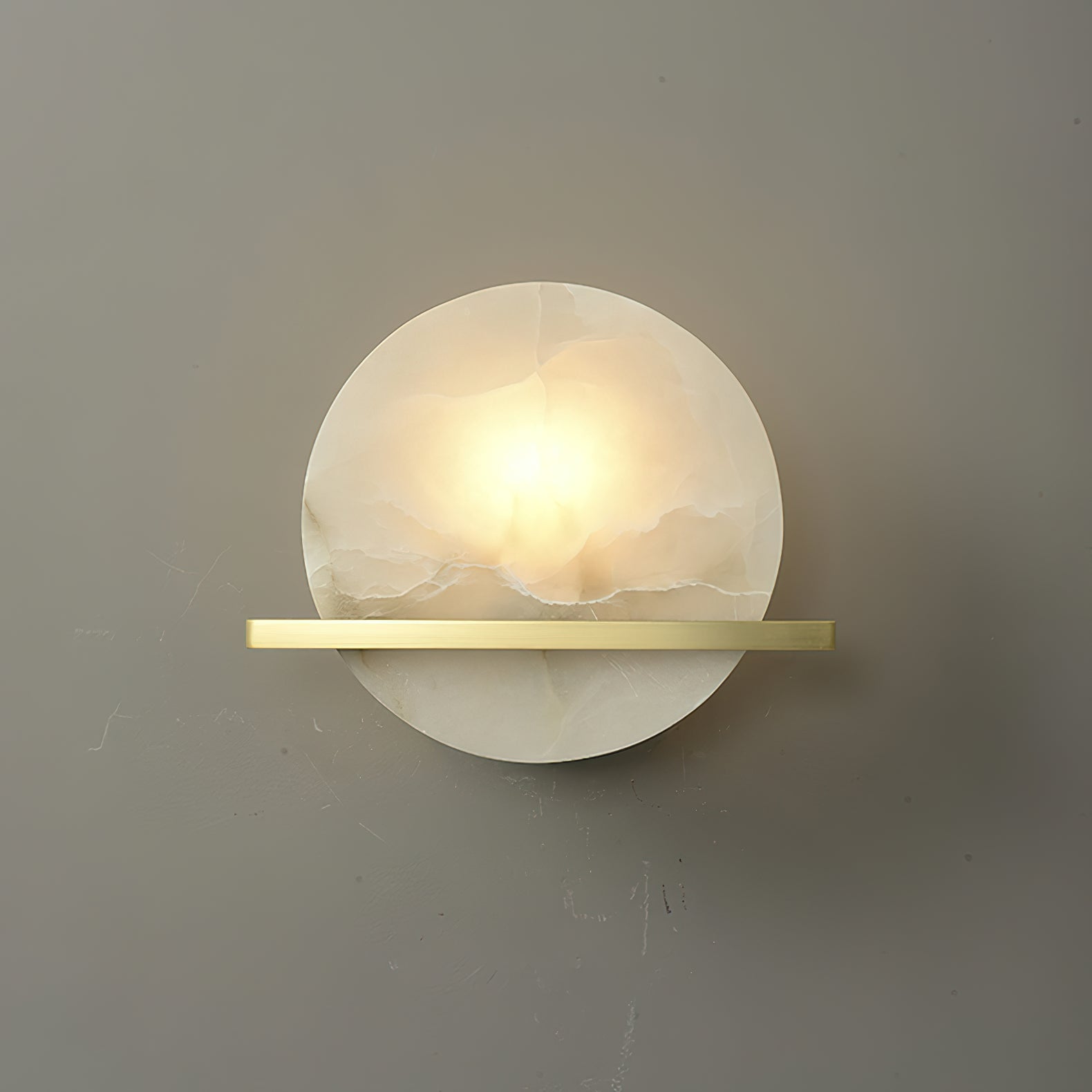 Clérachic White Alabaster Wall Sconce lit on a plain grey wall, the warm centre fading out to cooler white at the disc edges.