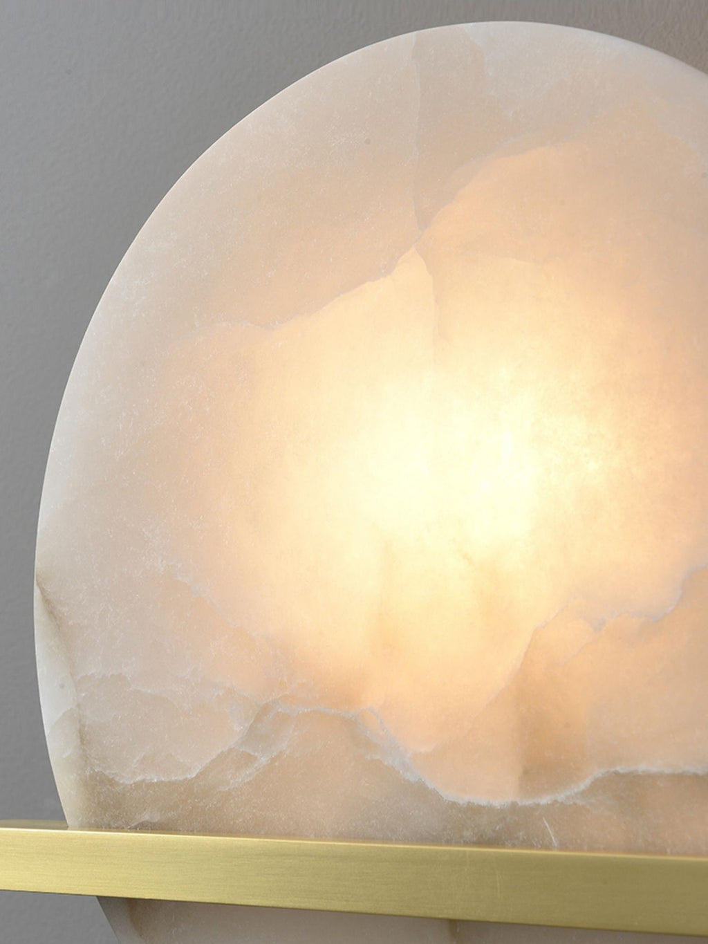 Macro of the Clérachic White Alabaster Wall Sconce shade, warm light spreading through the veined stone above the brass bar.