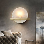 Clérachic White Alabaster Wall Sconce seen straight on in a grey concrete-walled lounge, glowing above a tufted velvet sofa.