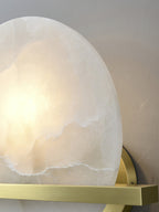 Detail of the Clérachic White Alabaster Wall Sconce against a pale wall, the lit disc edge showing how thick the stone is cut.