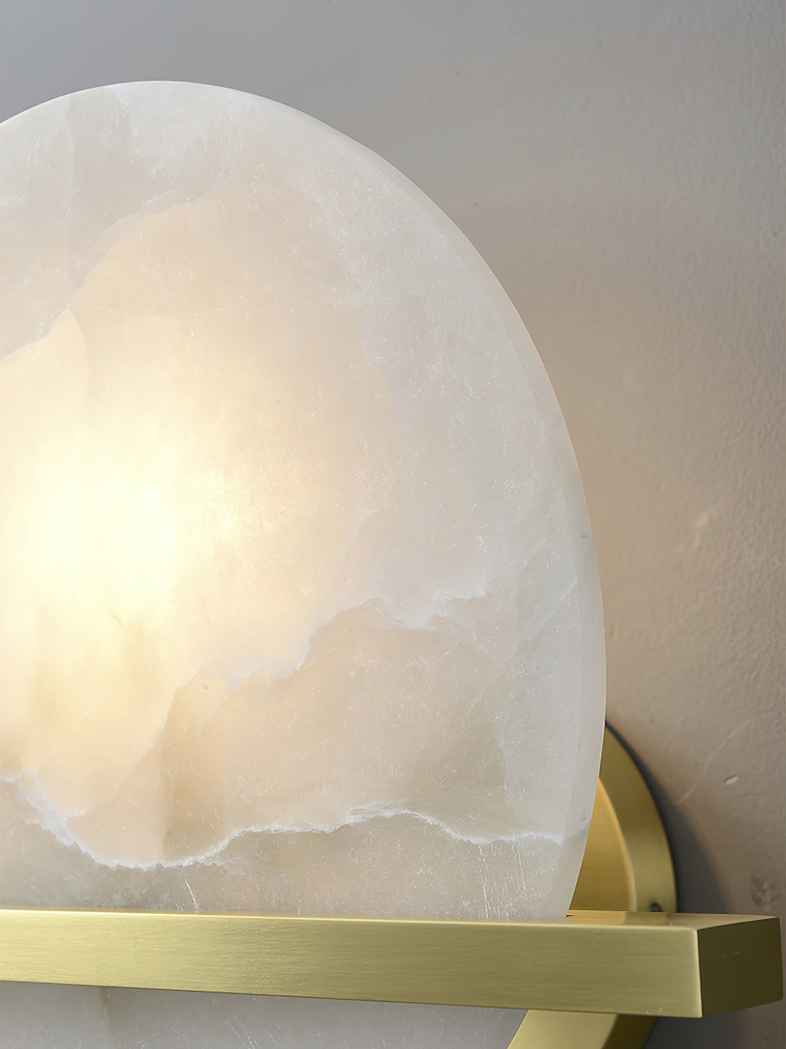 Detail of the Clérachic White Alabaster Wall Sconce against a pale wall, the lit disc edge showing how thick the stone is cut.