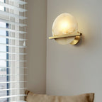 Clérachic White Alabaster Wall Sconce on a corner wall beside a blind-covered window, glowing over a linen window seat.