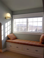 Clérachic White Alabaster Wall Sconce lit above a plaid window seat in a bright bedroom nook with a hillside view outside.