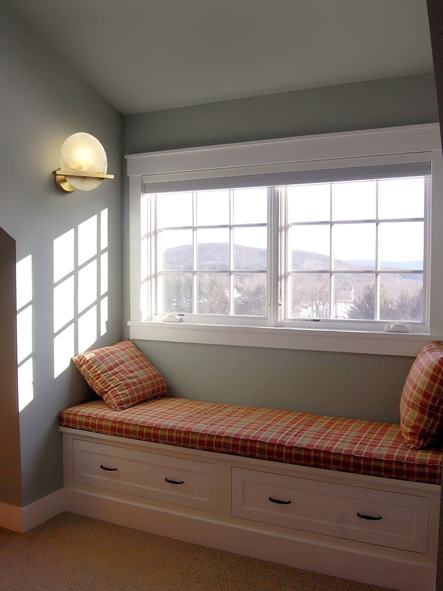 Clérachic White Alabaster Wall Sconce lit above a plaid window seat in a bright bedroom nook with a hillside view outside.