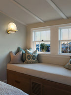 Clérachic White Alabaster Wall Sconce lit in a beamed bedroom, throwing a soft pool of light over the cushioned window seat.