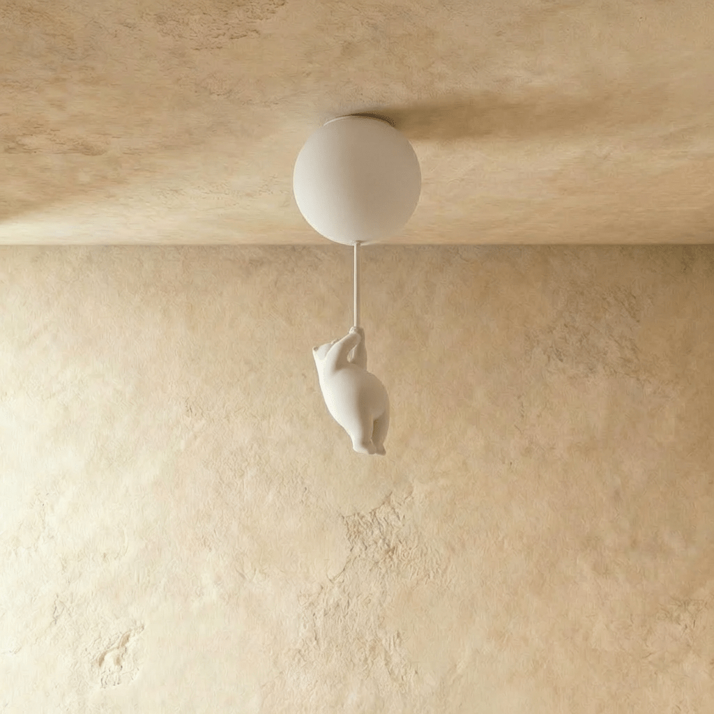 Clérachic bear-shaped figurine hangs from a cord below a single frosted glass globe against a warm plaster wall.