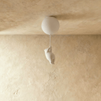 Clérachic bear-shaped figurine hangs from a cord below a single frosted glass globe against a warm plaster wall.