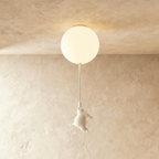 Clérachic white bear figurine hangs by its paws from a cord under a softly lit frosted glass ceiling globe.
