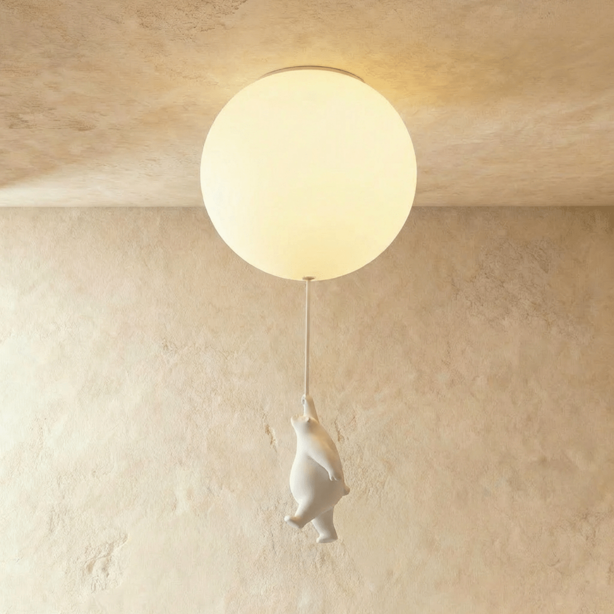 Clérachic white ceramic bear dangles from a cord below one frosted glass globe on a warm plaster ceiling.