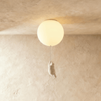 Clérachic ceiling light globe glows softly above a white bear figurine hanging by its front paws on the cord.