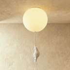 Clérachic ceramic bear figurine hangs low on its cord beneath a single glowing globe against a plaster wall.