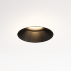 Clérachic trimless downlight glowing warm white from its black cone, the round housing sitting flush against the ceiling.