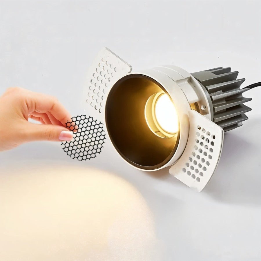 A hand fits the honeycomb anti-glare mesh into the Clérachic trimless downlight's illuminated black cone before final install.