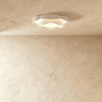 Clérachic compact ruffle-edged white ceiling light with a frosted diffuser, glowing softly on a textured plaster ceiling.