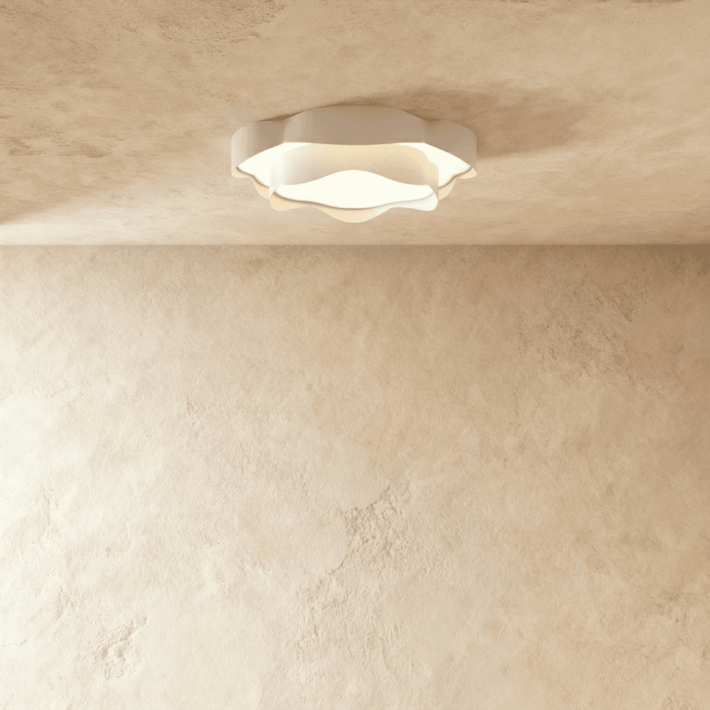 Clérachic low-profile white ceiling light with ruffled edges, glowing warm on a pale textured ceiling above a limewash wall.