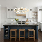 Clérachic ring chandelier with white petal shades above a navy kitchen island with three rattan stools and a white kitchen behind.