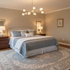 This Clérachic chandelier, a branching gold arm with white petal shades, hangs above a made bed with blue bedding in a taupe bedroom.